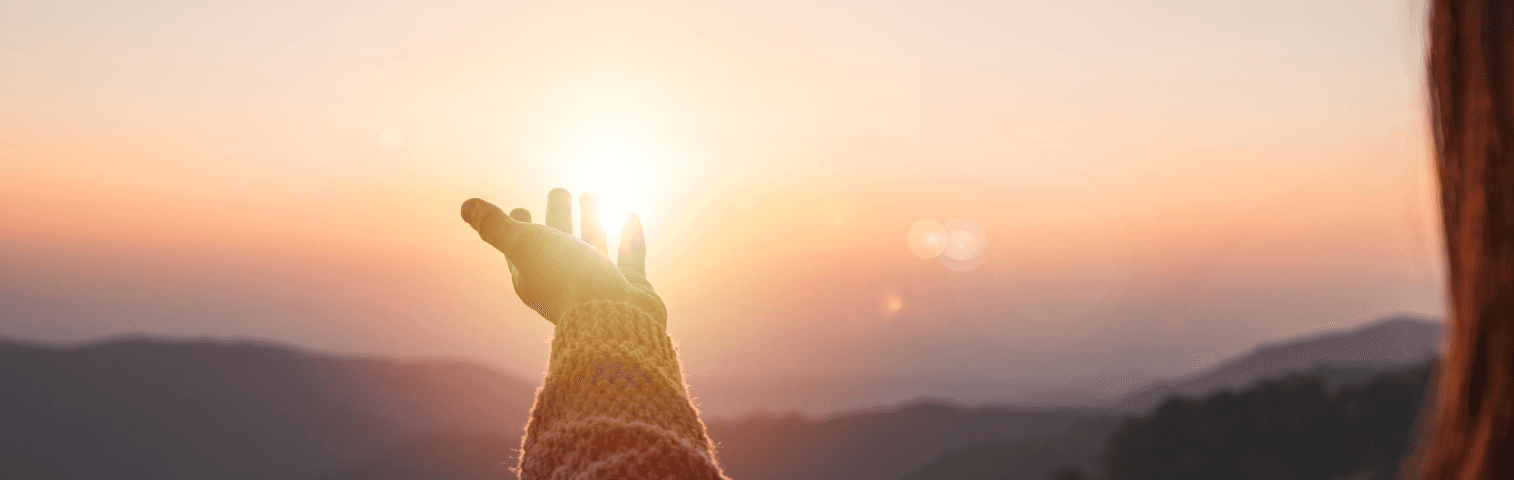 Hand im Sonnenaufgang über Bergen, warmes Morgenlicht – Inspiration, Achtsamkeit und Neubeginn in der Natur